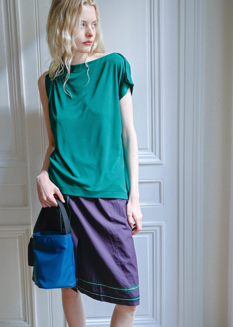 Side view of the blue Orsi nylon bucket bag by TURN Paris, worn with a green top