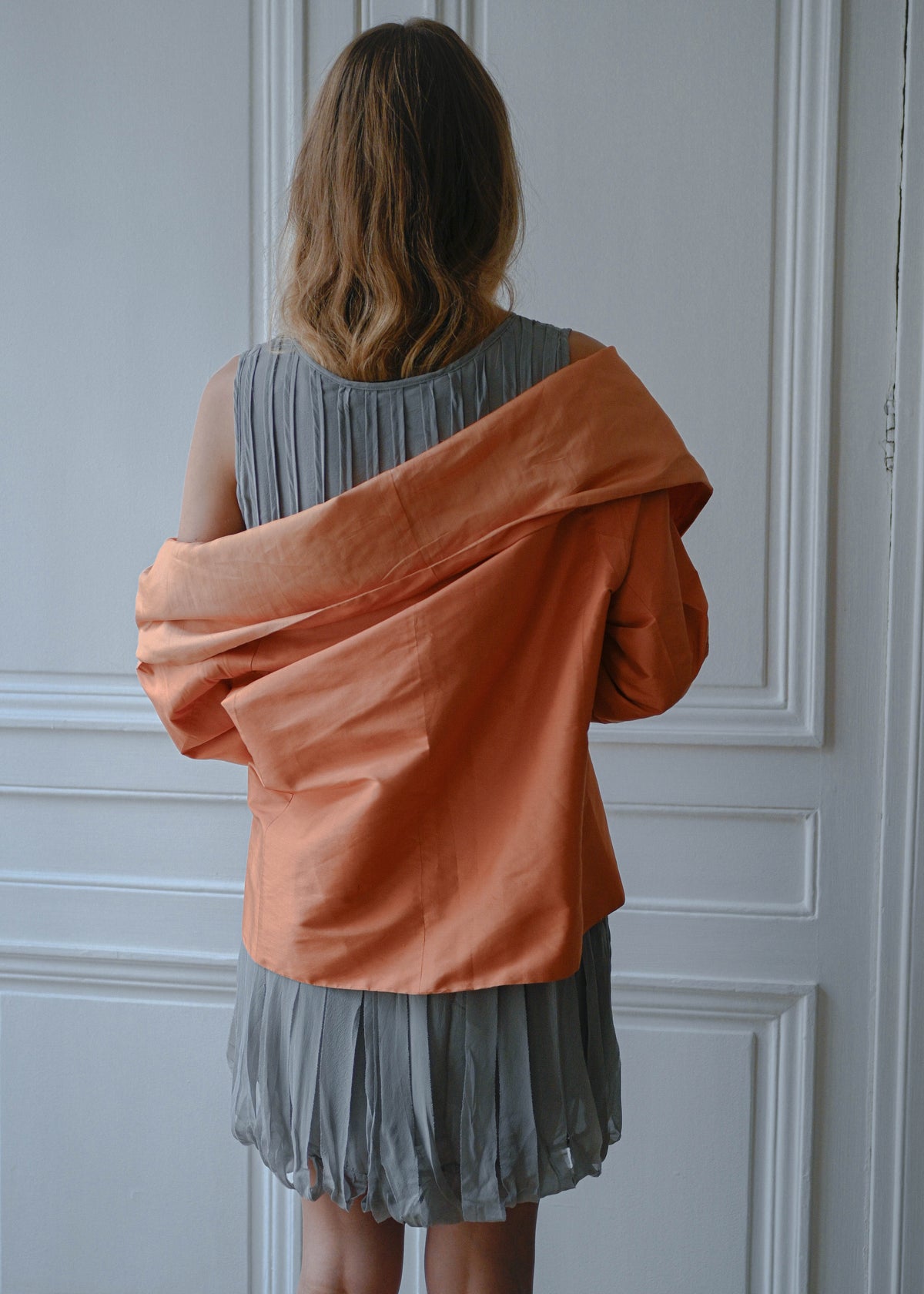 Orange draped silk jacket worn over grey silk fringe dress, back view