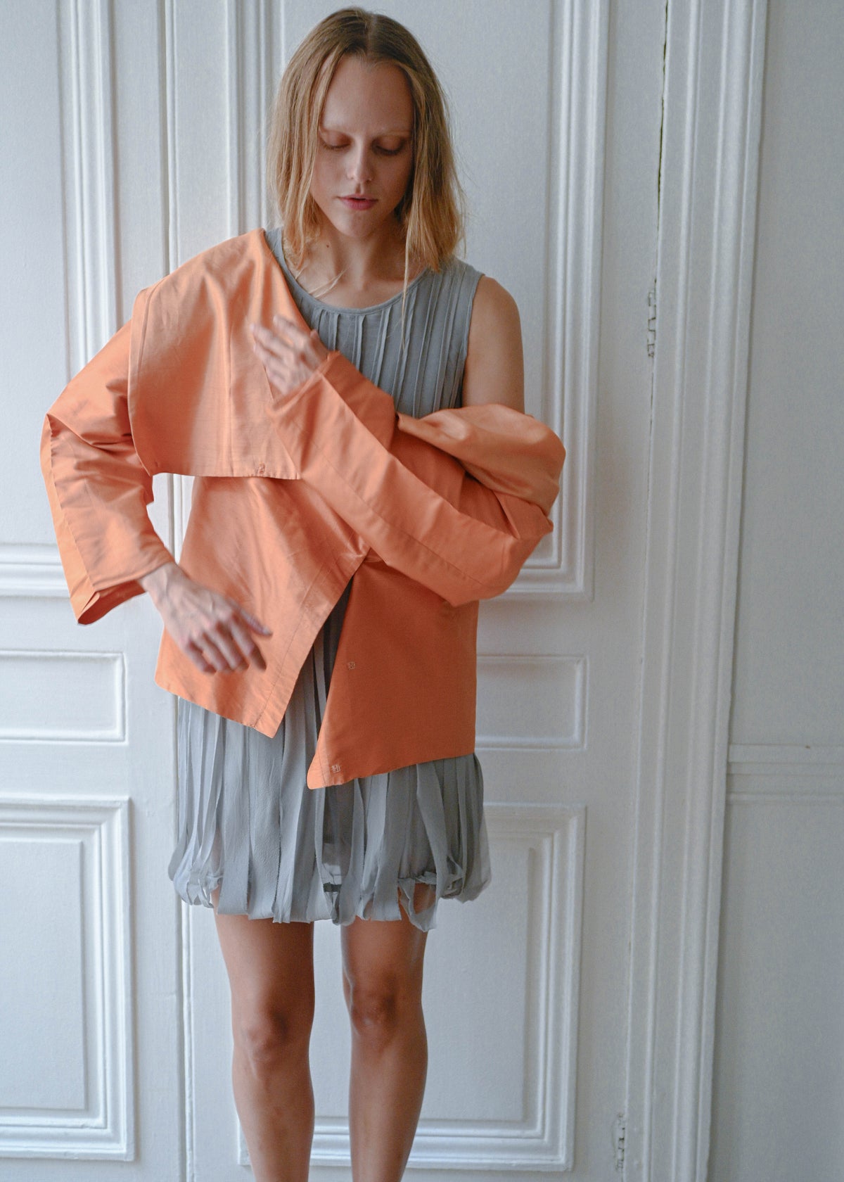 Orange draped silk jacket worn over grey silk fringe dress, close-up