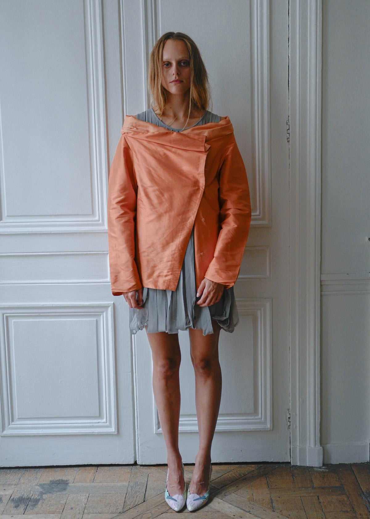 Orange draped silk jacket worn over grey silk fringe dress, front view
