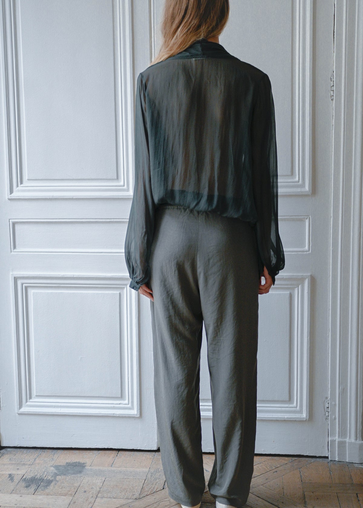 Green sheer draped blouse worn with grey trousers, back view
