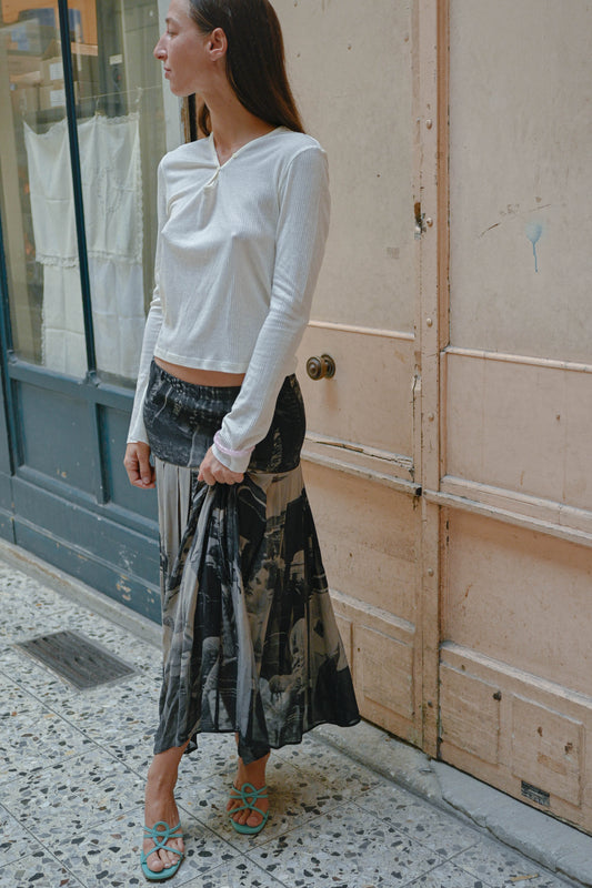 Model wearing the TURN Paris White Tunisien Top, a fine long sleeve knit with V neckline, with a printed pleated maxi skirt