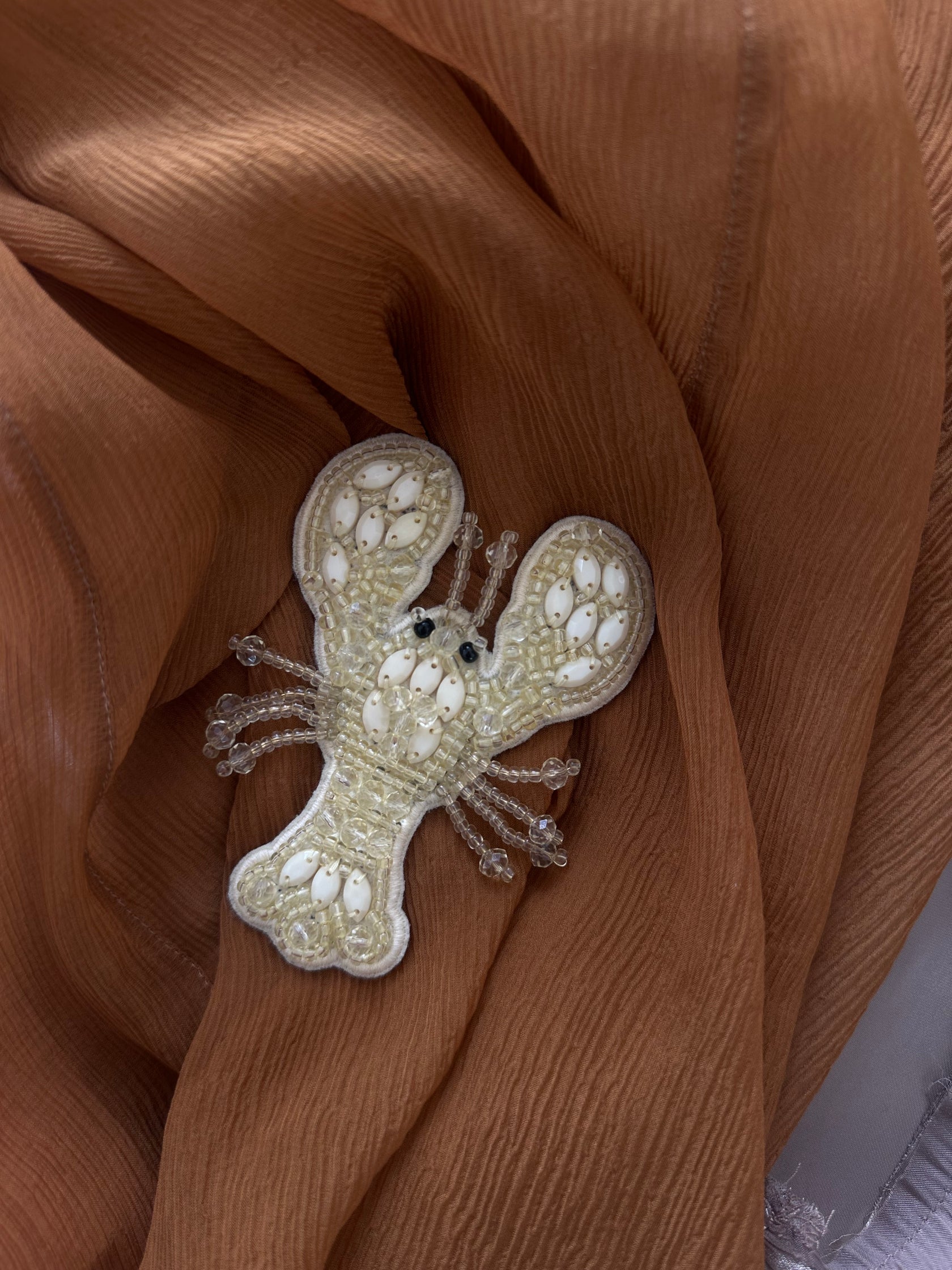 TURN PARIS lobster brooch in cream, embroidered with beads and gemstone embellishments across the body and claws.

Designed with a flat base and metal pin at the back, to be worn on a bag, jacket or shoe.

10 cm length.